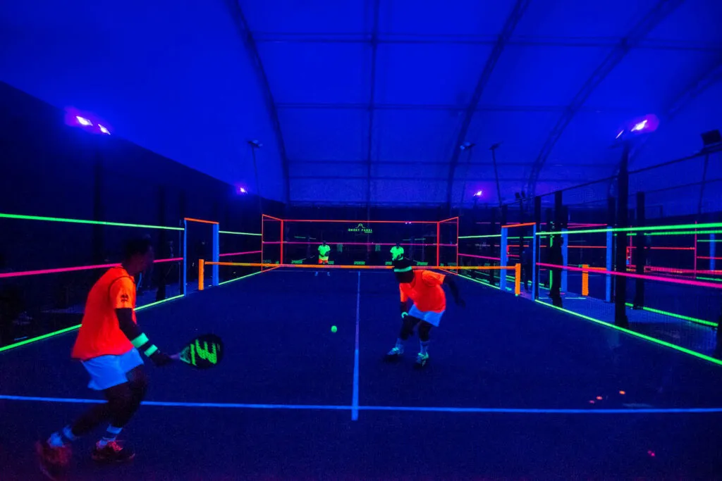 Padelspiel unter Schwarzlicht, leuchtende Linien auf dem Platz